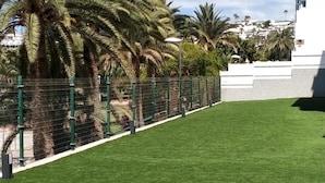 Zona verde y bien cuidada con cerca verde y palmeras, probablemente parte de una propiedad de resort o hotel.