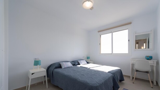 Un dormitorio con cama, escritorio, silla, ventana y mesita de noche.