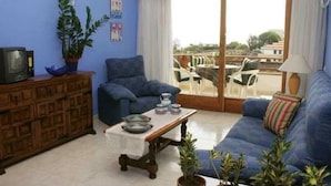 Un salón con un sofá azul, un armario de madera, una mesa con platos y vistas al balcón exterior.