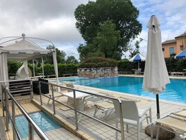 Una piscina con lettini e ombrelloni, immersa nel verde e delimitata da un muro in pietra.