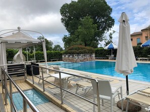 Una piscina con sillas de descanso y sombrillas, rodeada de vegetación y un muro de piedra.