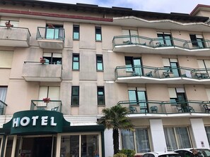 Un hotel de diversos pisos amb balcons, un rètol que indica que és un hotel i una palmera al davant.
