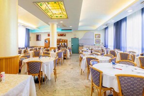 A spacious dining area with multiple tables and chairs, a central column, and a decorative ceiling light. - Harrys (Jesolo)