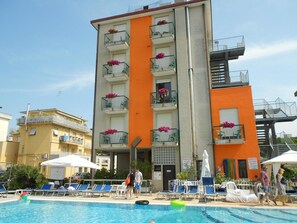 Hotel amb piscina, diversos balcons amb testos de flors i un senyal de precaució de socorrista.