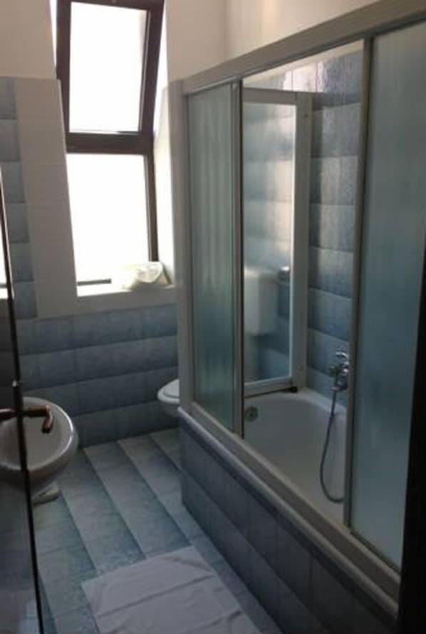 Un baño con ducha de mampara de vidrio, inodoro y lavamanos.