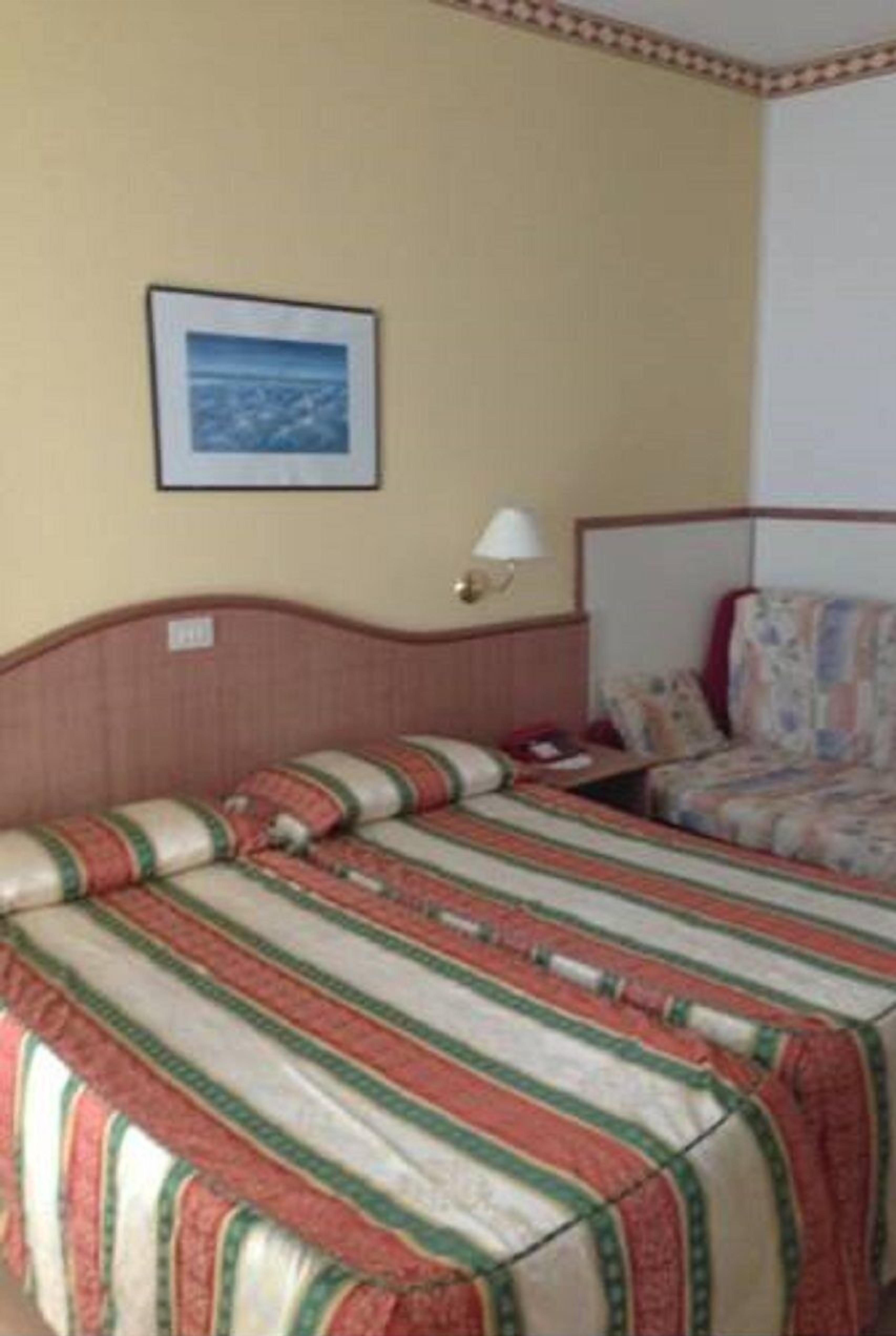 Ein Hotelzimmer mit zwei Betten, einem gerahmten Bild an der Wand und einem Nachttisch mit Lampe.