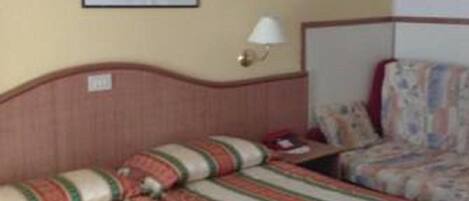 Una habitación de hotel con dos camas, un cuadro enmarcado en la pared y una mesita de noche con una lámpara.