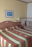 Una camera d'albergo con due letti, un quadro appeso al muro e un comodino con una lampada.