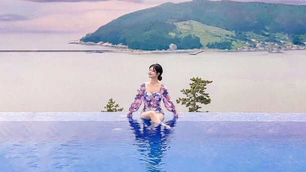 A person sitting in a pool with a view of a body of water and hills in the background.
