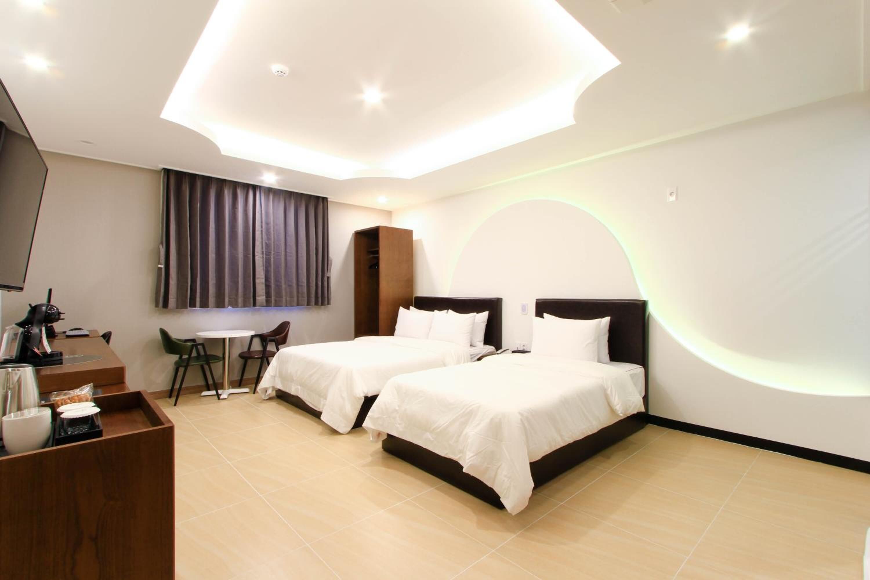 Quarto de hotel com duas camas, uma escrivaninha com cadeira, televisão e uma pequena mesa com bandeja.