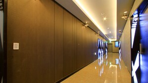 A long, well-lit hallway with a polished floor and dark walls, leading to a door with a digital display. - The King Hotel (Busan)