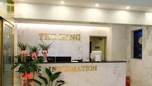 A reception desk with "THE KING" and "INFORMATION" signage, a coffee machine, and potted plants. - The King Hotel (Busan)