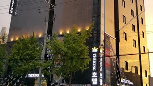 A modern hotel building with a reflective glass facade, multiple floors, and a prominent crown logo. - The King Hotel (Busan)