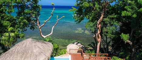 A wooden deck with a pool, surrounded by lush greenery and overlooking a clear blue sea.