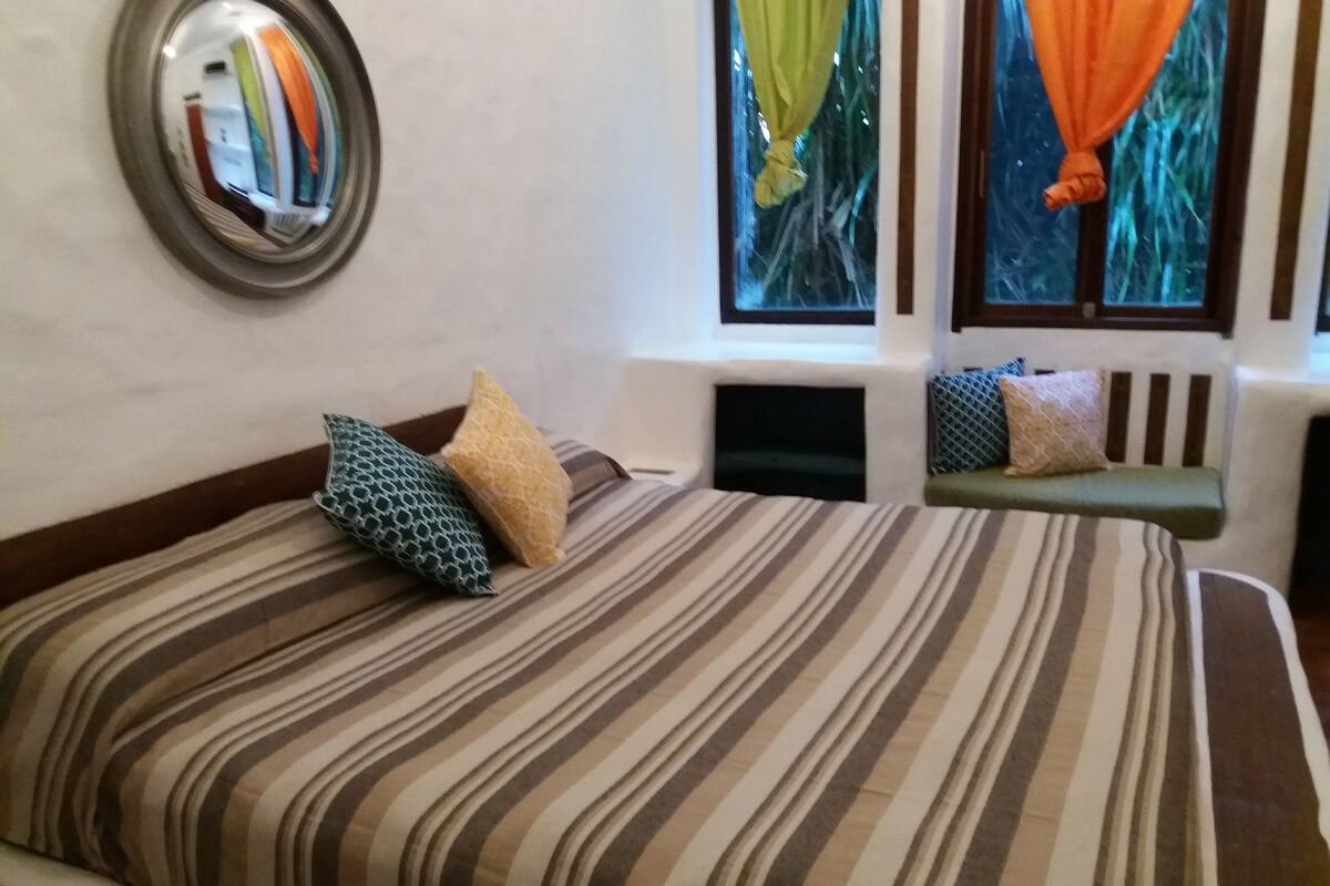 A hotel room with a striped bedspread, a bedside table with a lamp, and a window with curtains.