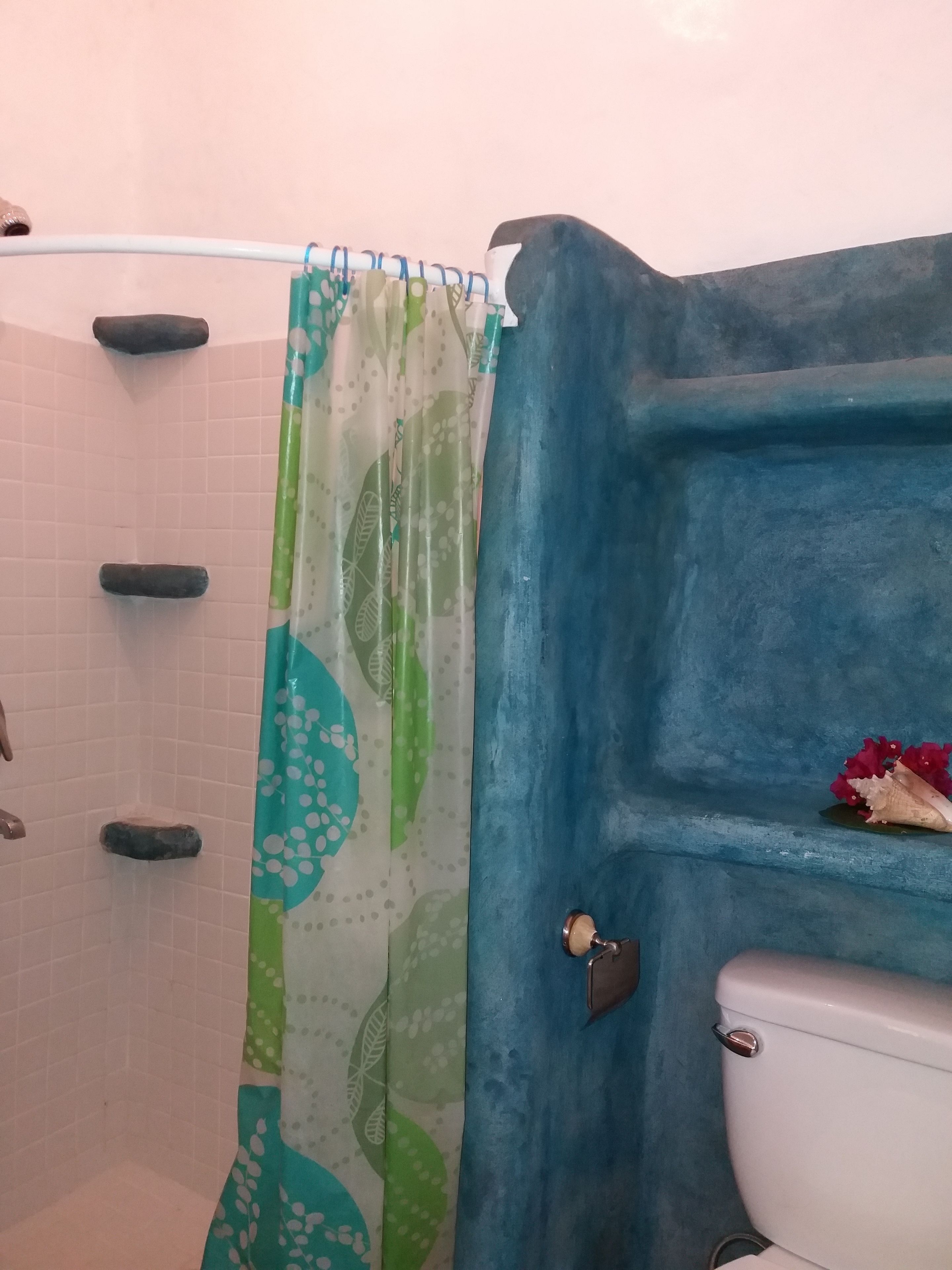 A bathroom with a shower curtain, a toilet, and a shelf with a decorative item.