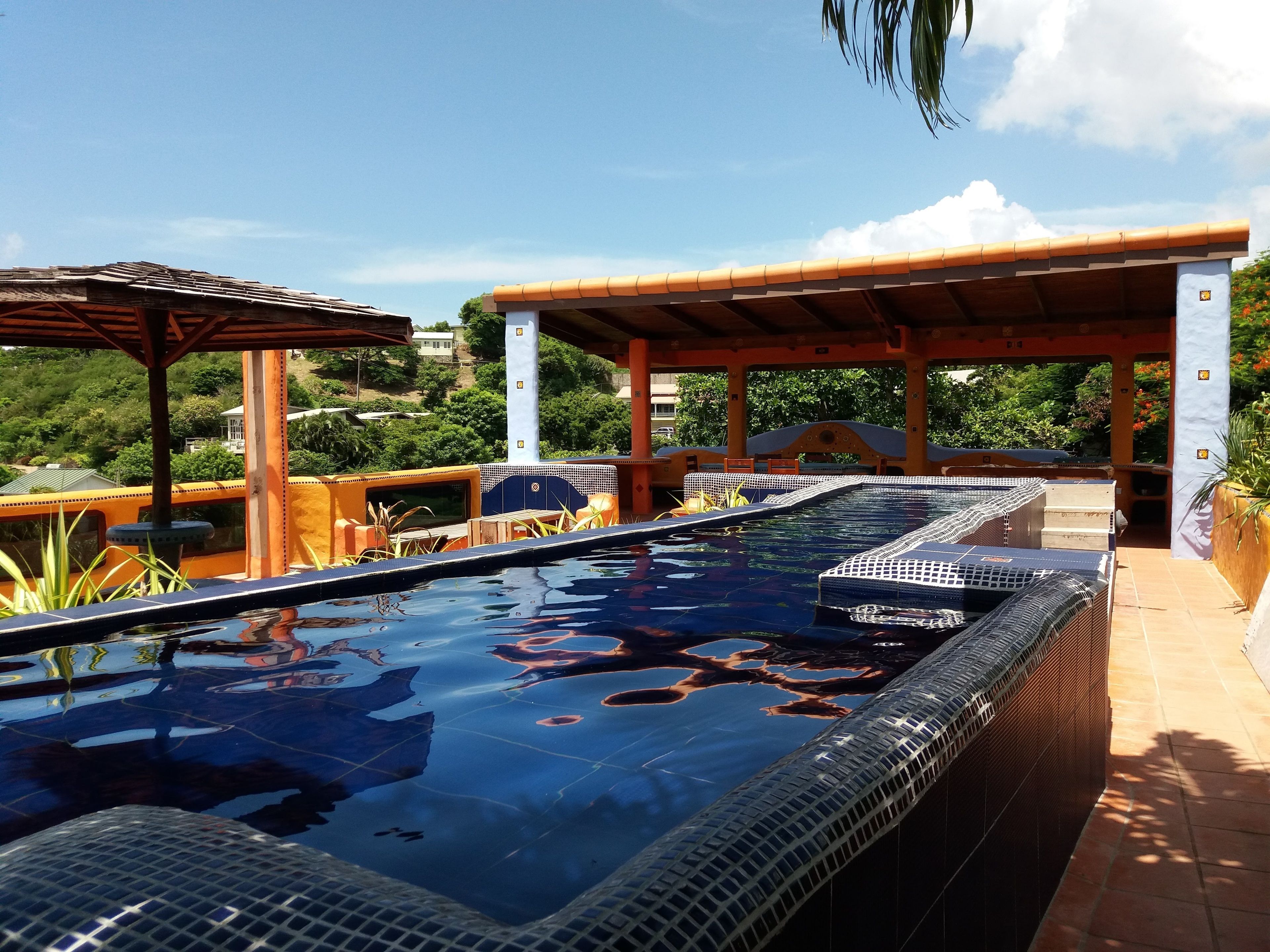 A swimming pool with a tiled deck, surrounded by a covered patio area with seating.