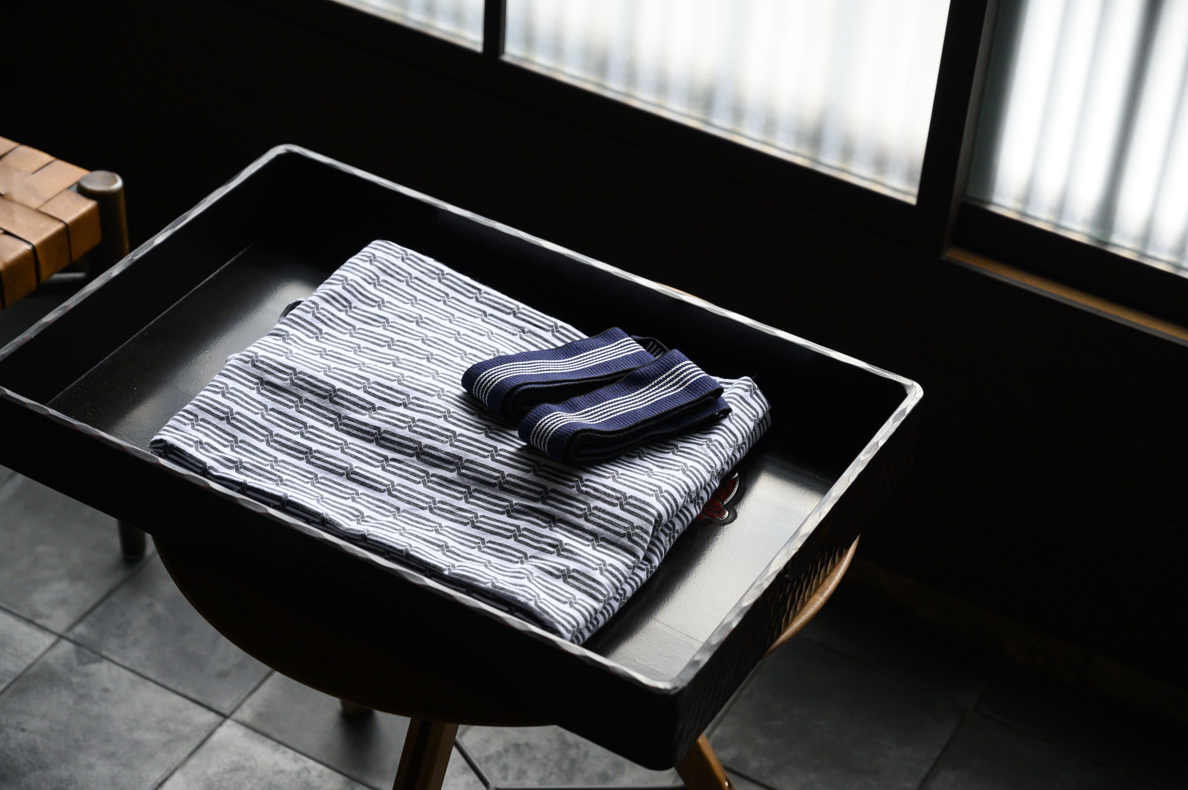 A neatly folded striped towel on a black tray table in a modern room with a window.