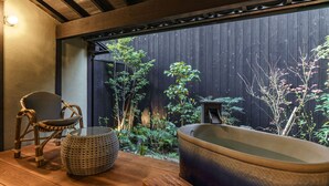 Eine Holzterrasse mit einer großen Badewanne, einem Korbstuhl und einem gewebten Hocker.