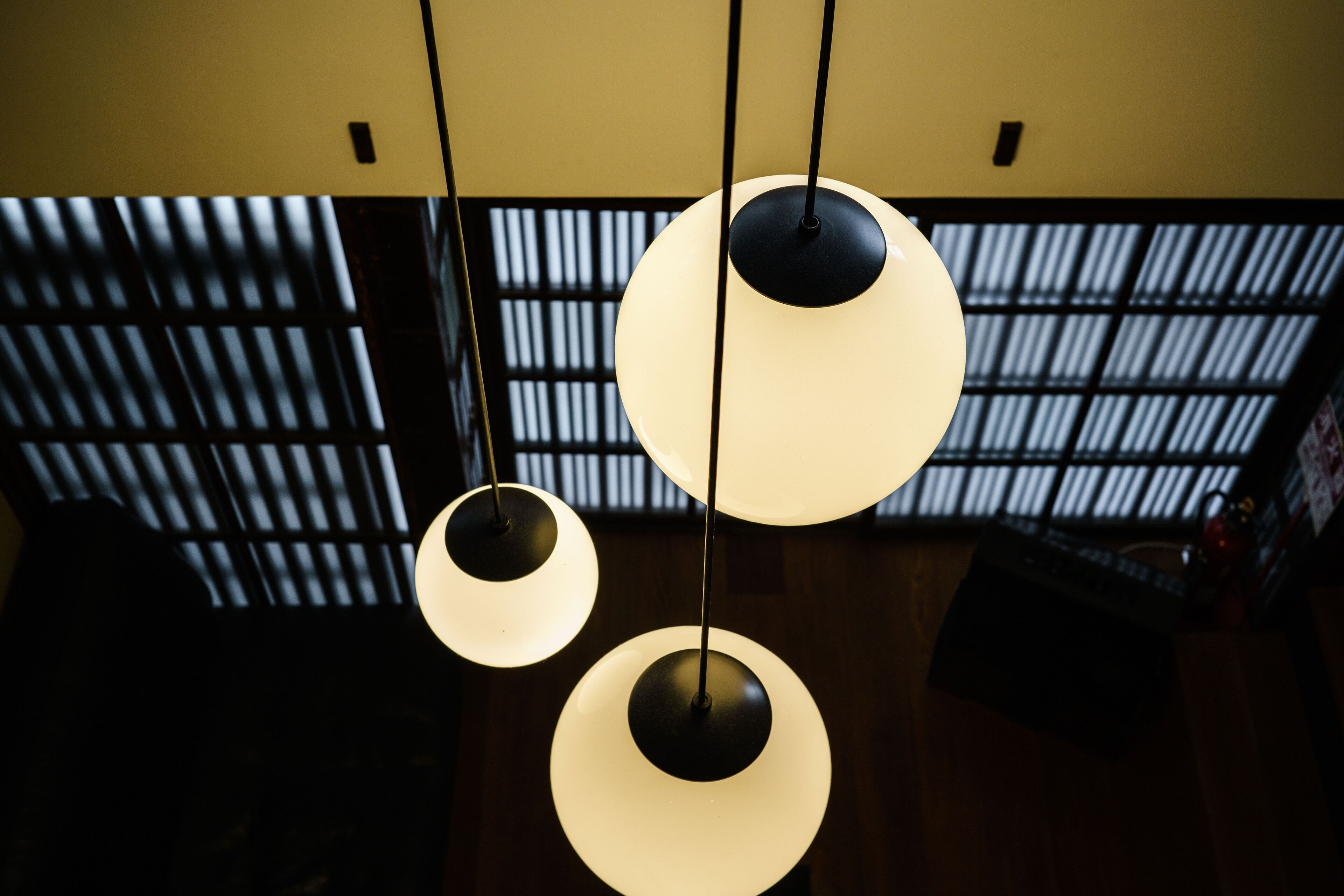 Three pendant lights hanging from the ceiling in a room with a dark wooden floor and a window with vertical blinds.