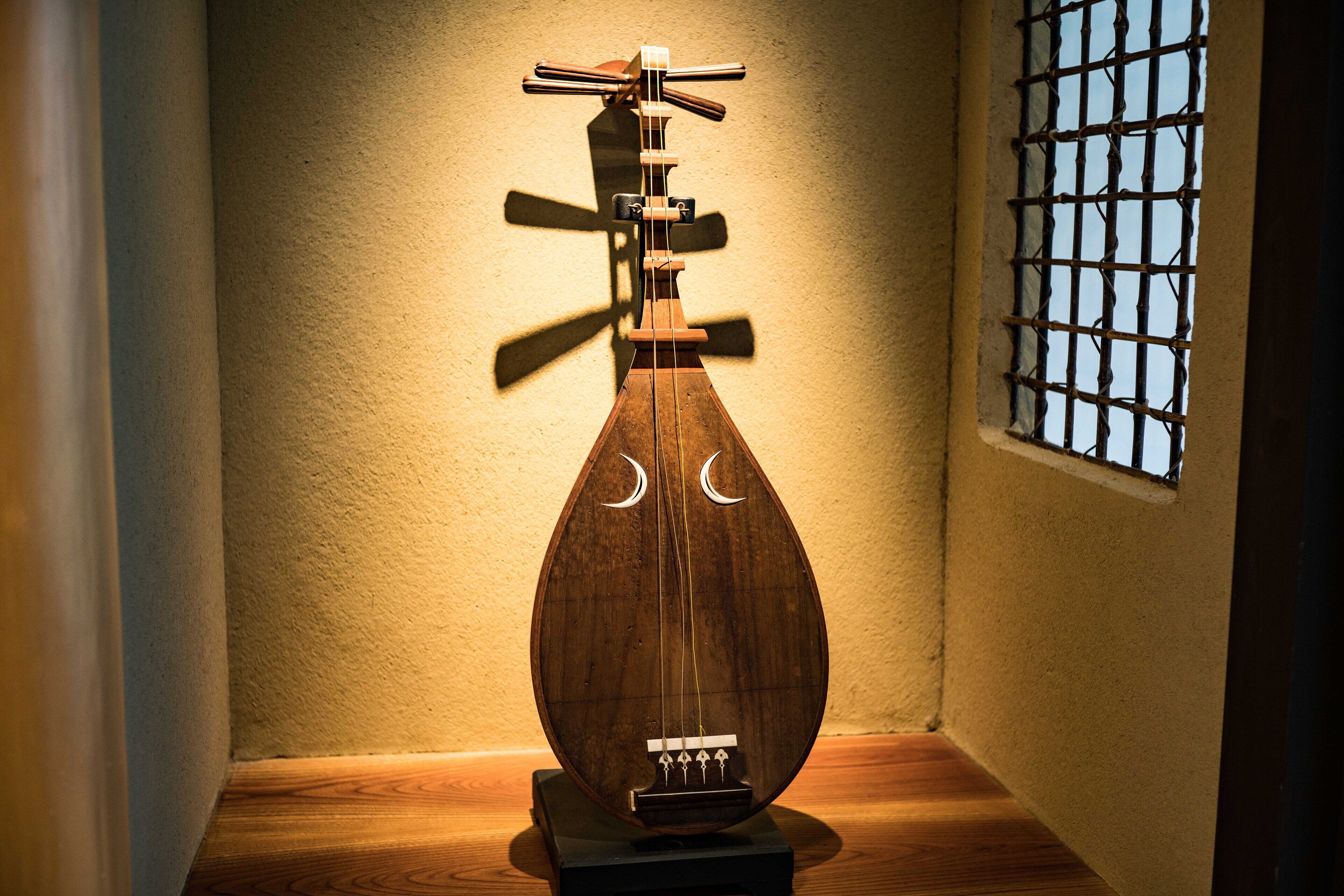 A traditional stringed musical instrument displayed against a textured wall with a barred window.