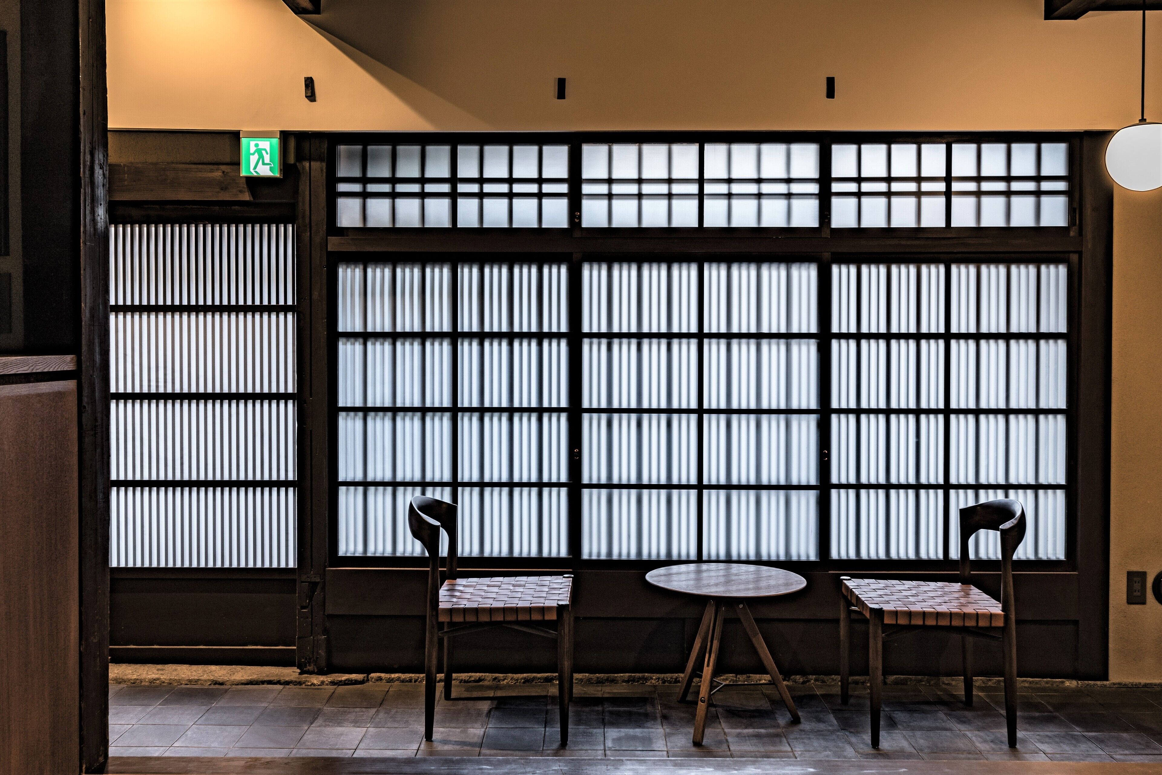 A traditional Japanese room with tatami flooring, a shoji screen, two wooden chairs, and a small round table.