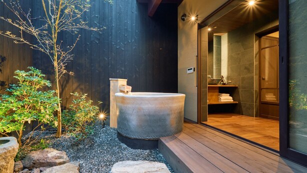 Ein modernes Badezimmer im Freien mit einer Stein-Hot Tub, umgeben von Steinen und Grünpflanzen.