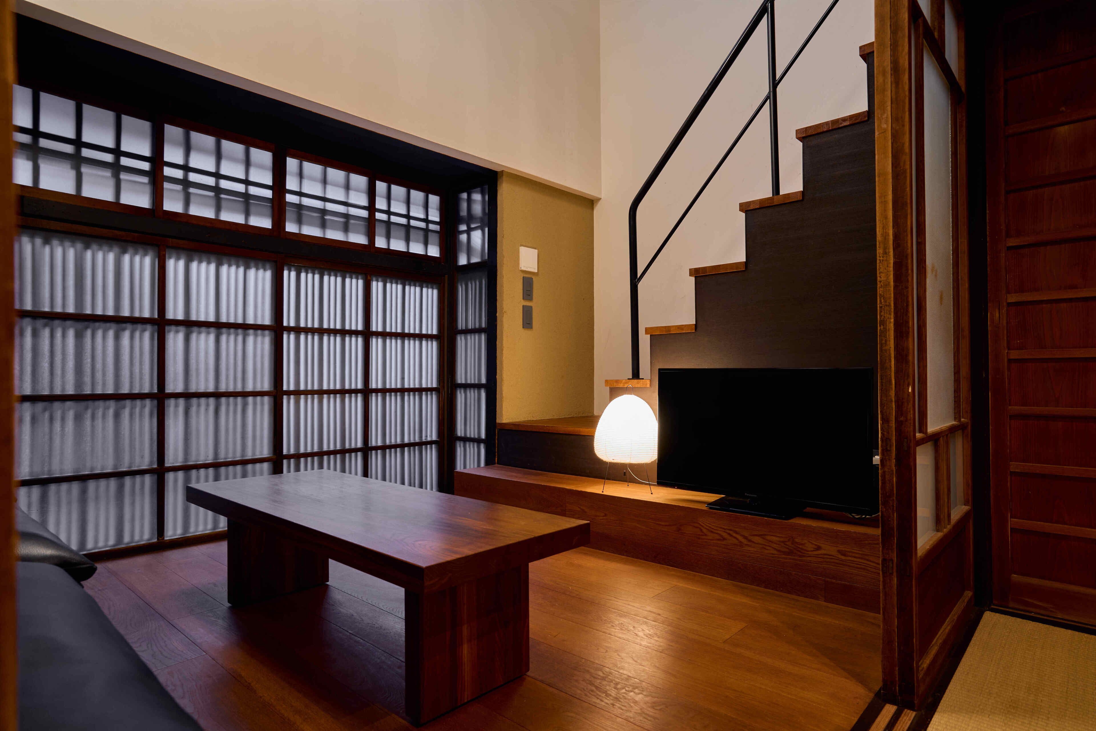 A modern interior with a wooden bench, a TV on a low stand, and a staircase.