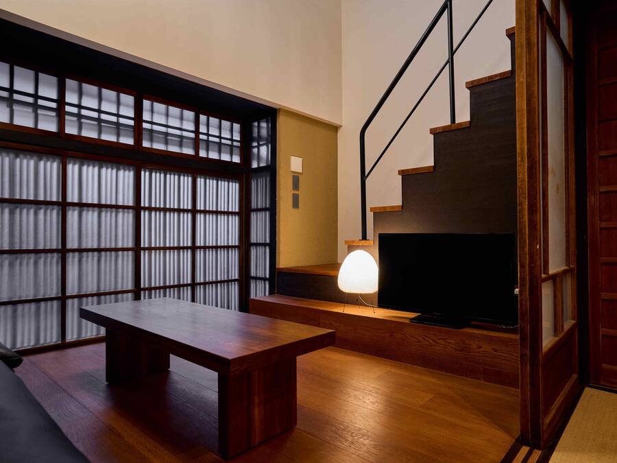 A modern interior with a wooden bench, a TV on a low stand, and a staircase.