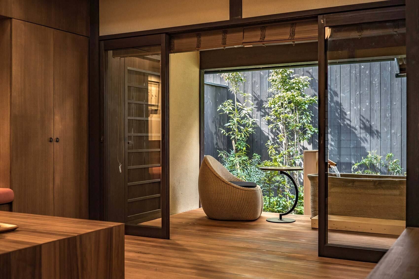A modern interior with a sliding glass door leading to a backyard with plants and a wicker chair.