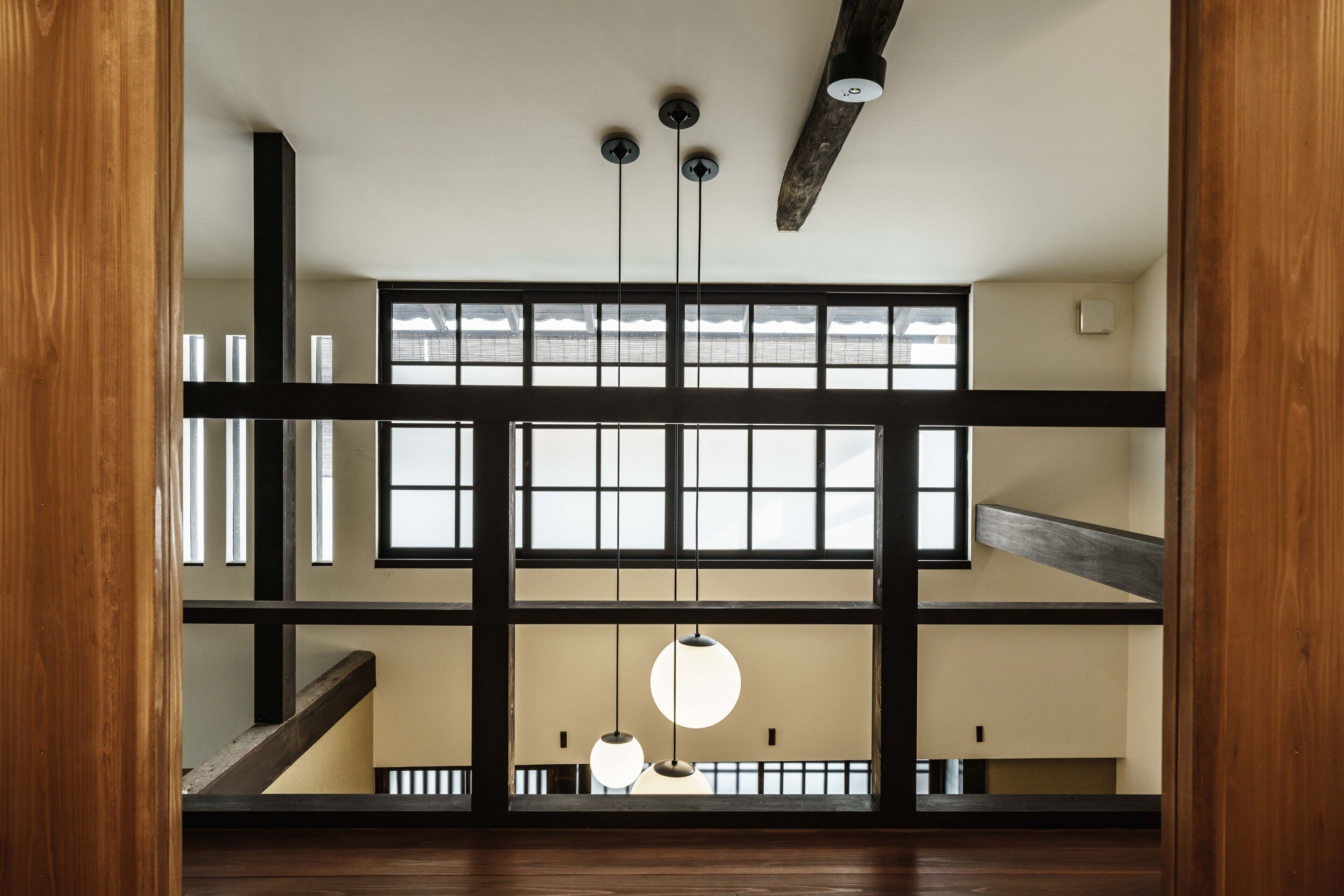 A multi-level interior with wooden beams, large windows, and hanging pendant lights.