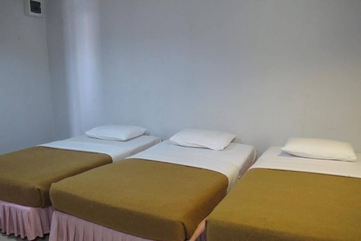 Ein Zimmer mit drei Einzelbetten, jedes mit einer weißen Matratze und einer braunen Decke.