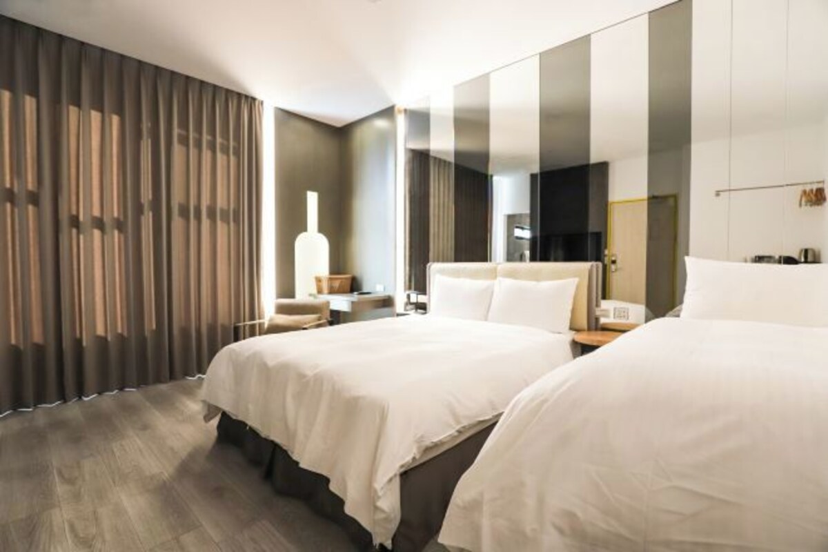 A modern hotel room with two beds, a large mirror, and a wooden floor.