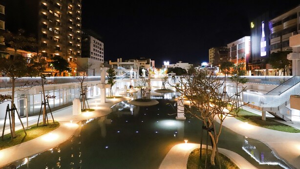 A nighttime view of a modern urban area with a central water feature, illuminated pathways, and surrounding buildings. - Hotel Initial-Beer (Tainan)