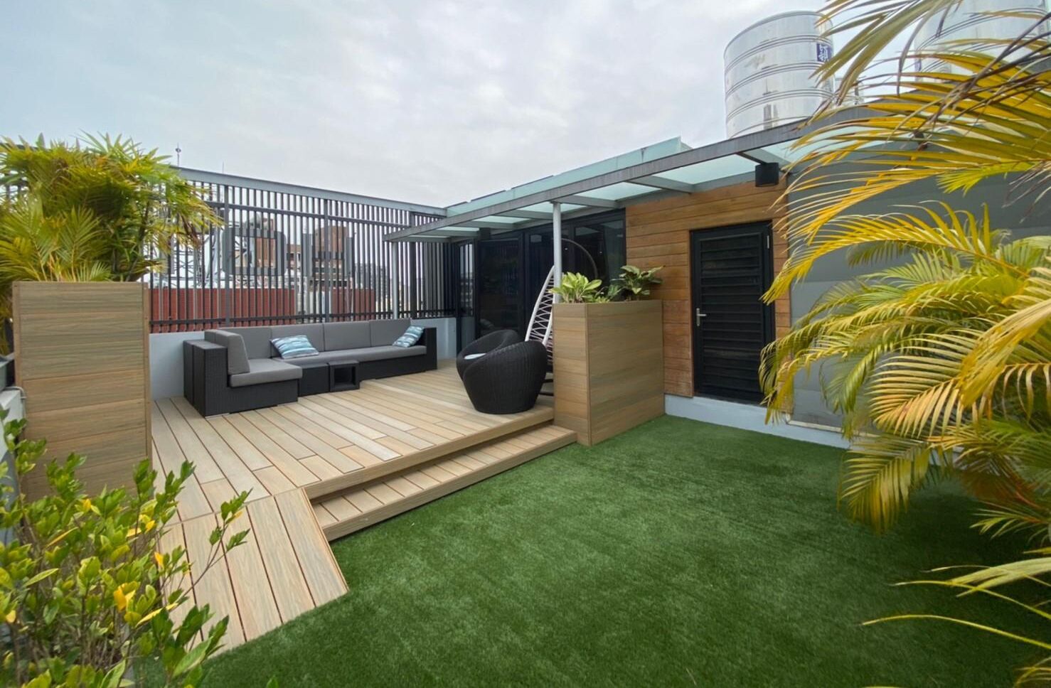 A modern outdoor patio with a wooden deck, a hanging chair, and a built-in seating area.