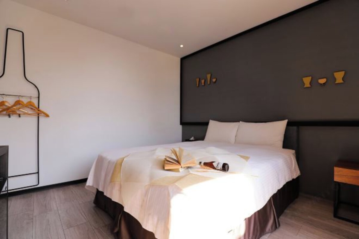 A modern hotel room with a large bed, a bedside table, and a wall-mounted coat rack.