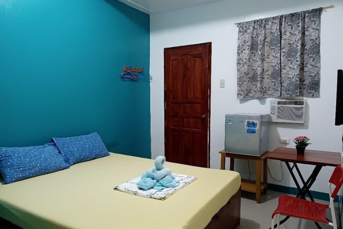 A room with a bed, a desk, a chair, an air conditioner, and a door.