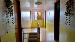 A hallway with a metal bench, a window with a view, and decorative plants on the walls. - Pete's Inn (Roxas City)