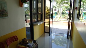 A hotel lobby with a reception desk, a chair, a small table with a hat and magazines, and a view of a pool and palm trees outside. - Pete's Inn (Roxas City)