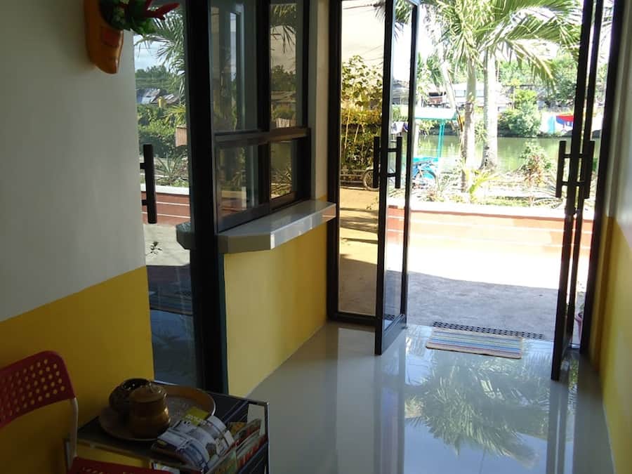A hotel lobby with a reception desk, a chair, a small table with a hat and magazines, and a view of a pool and palm trees outside.