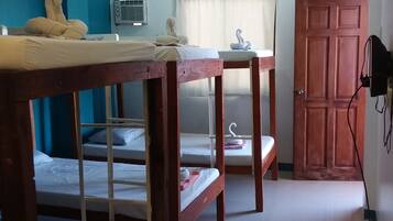 A dormitory room with bunk beds, a small table, a wardrobe, and a wall-mounted air conditioning unit.