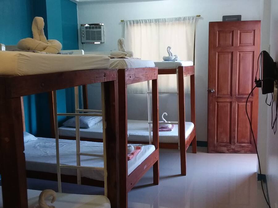 A dormitory room with bunk beds, a small table, a wardrobe, and a wall-mounted air conditioning unit.