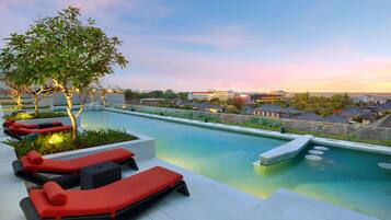 A rooftop pool area with lounge chairs and a tree.