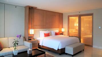 A hotel room with a large bed, a sofa, a coffee table, and a nightstand with a lamp.