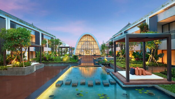 Un hotel moderno con piscina central, asientos exteriores y exuberante jardinería.