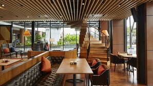 Un interior moderno con techo de madera, una escalera, una zona de estar con sofá y mesas, y vistas amplias a través de grandes ventanales.