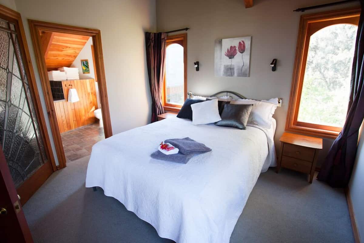 A neatly made bed with a white bedspread, a small bedside table, and a window with curtains.
