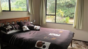 Quarto com uma janela grande, cabeceira de madeira e cama com colcha escura e várias almofadas.