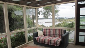 Um solário com vista para um lago, um sofá xadrez e uma mesa de madeira.
