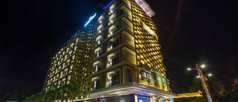 A multi-story hotel with illuminated signage, a parking area, and a flagpole.